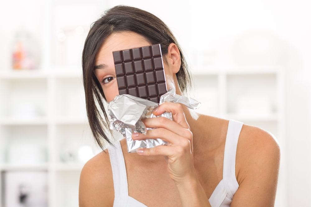 Woman holding a bar of dark chocolate in front of her face