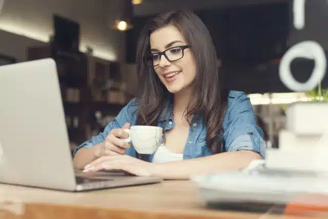 Woman drinking coffee and working on her laptop