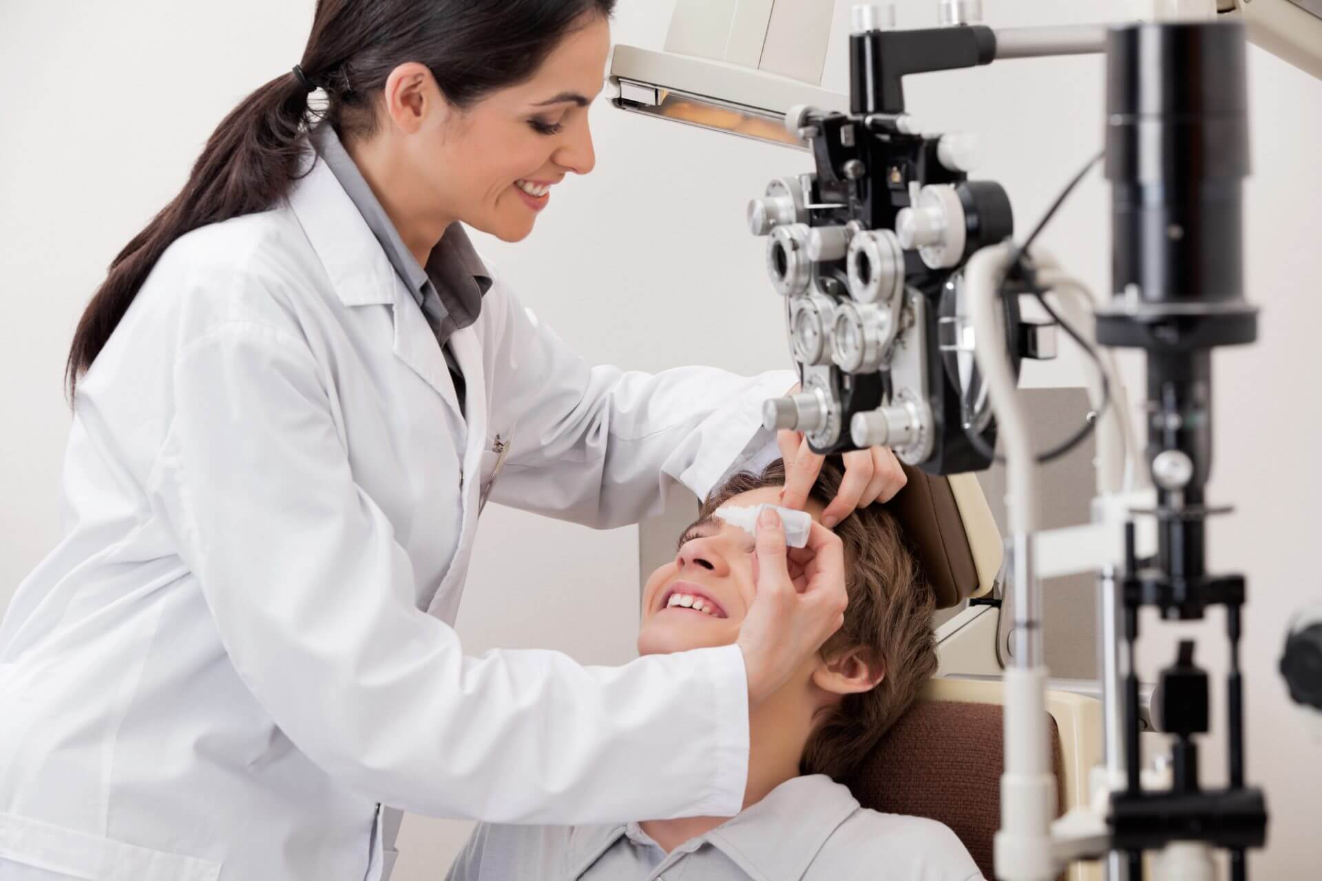 Young man smiling while the eye doctor puts eye drops in his eyes